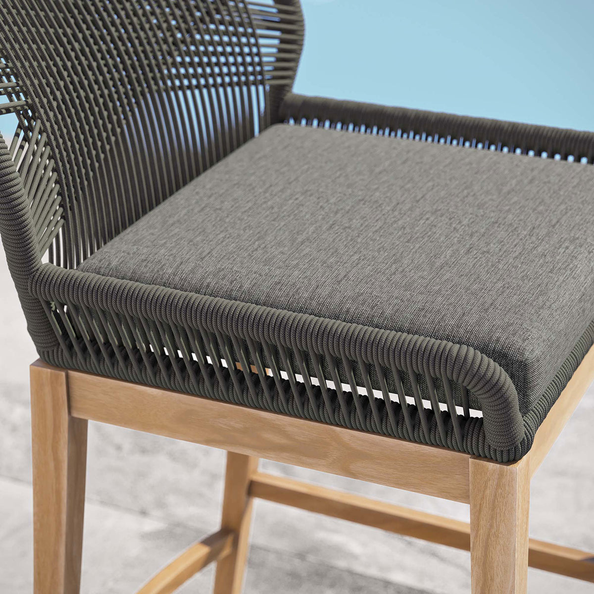 Soft gray cushion and tightly wrapped graphite rope frame on the Wellspring bar stool beside calm blue water. || EEI-5746-GRY-GPH || detail_room