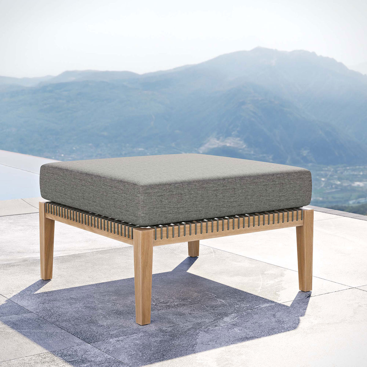 Graphite cushion teak patio ottoman overlooking a scenic view for a relaxing outdoor lounge || EEI-5854-GRY-GPH || front_angle_room