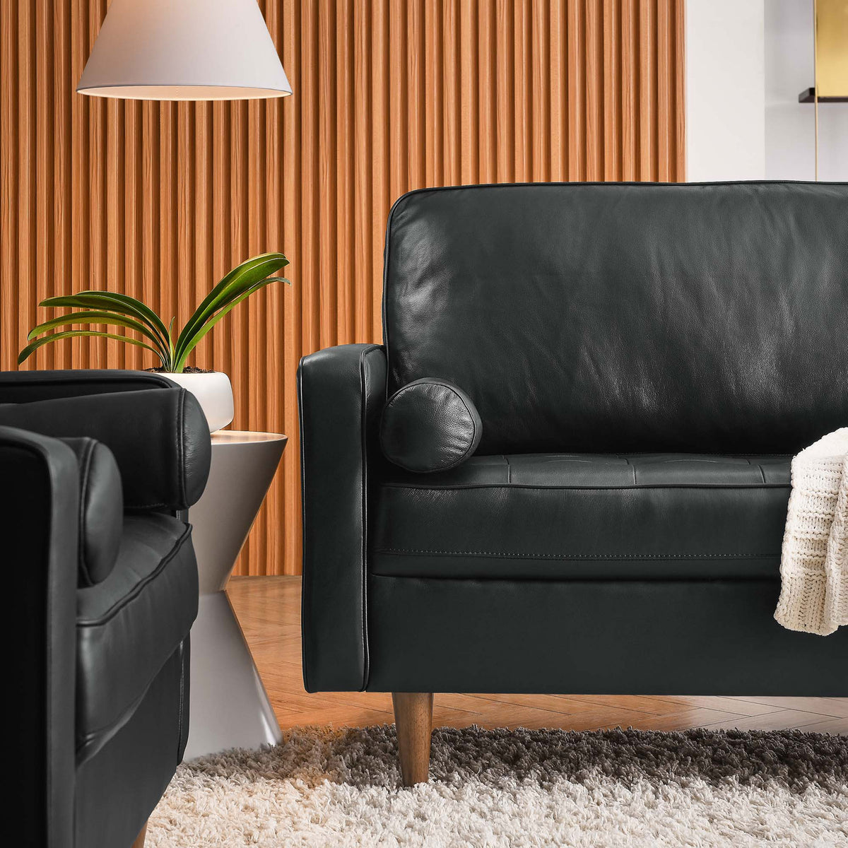 Black leather Valour sofa arm with bolster pillow pairs with cozy rug, accent chair, and floor lamp for a warm lounge. || EEI-5871-BLK || detail_room