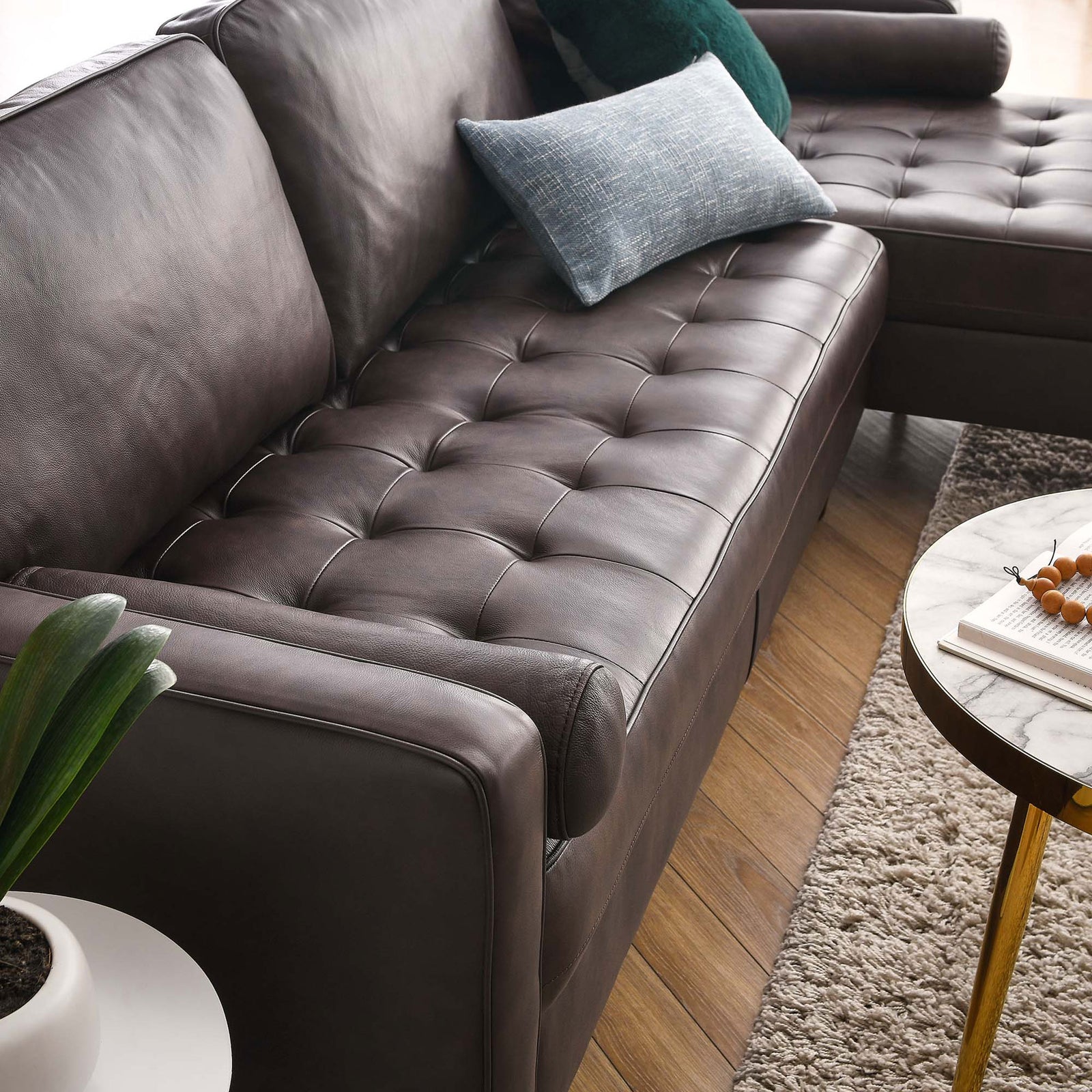 Tufted brown leather seat of the sectional with accent pillows beside a marble-top coffee table || EEI-5873-BRN || detail_room