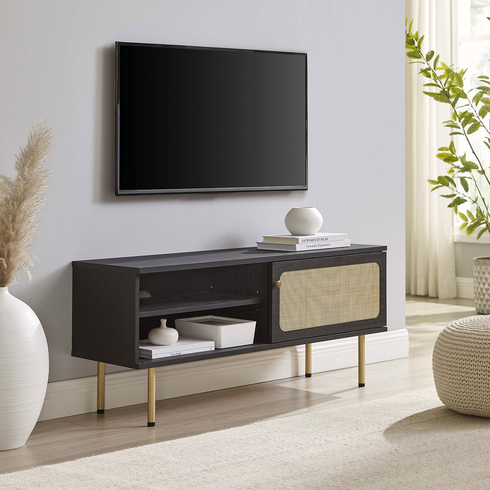 Black TV console with rattan sliding door and gold legs anchoring a neutral living room seating area. || EEI-6044-BLK || front_angle_room
