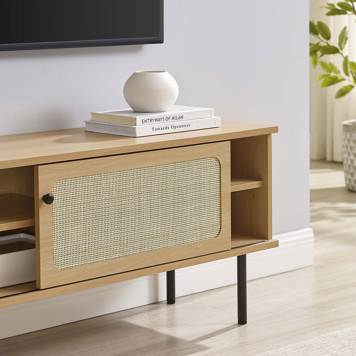 Oak rattan TV stand styled beneath a wall-mounted TV with books and decor in a bright room. || EEI-6044-OAK || storage_room