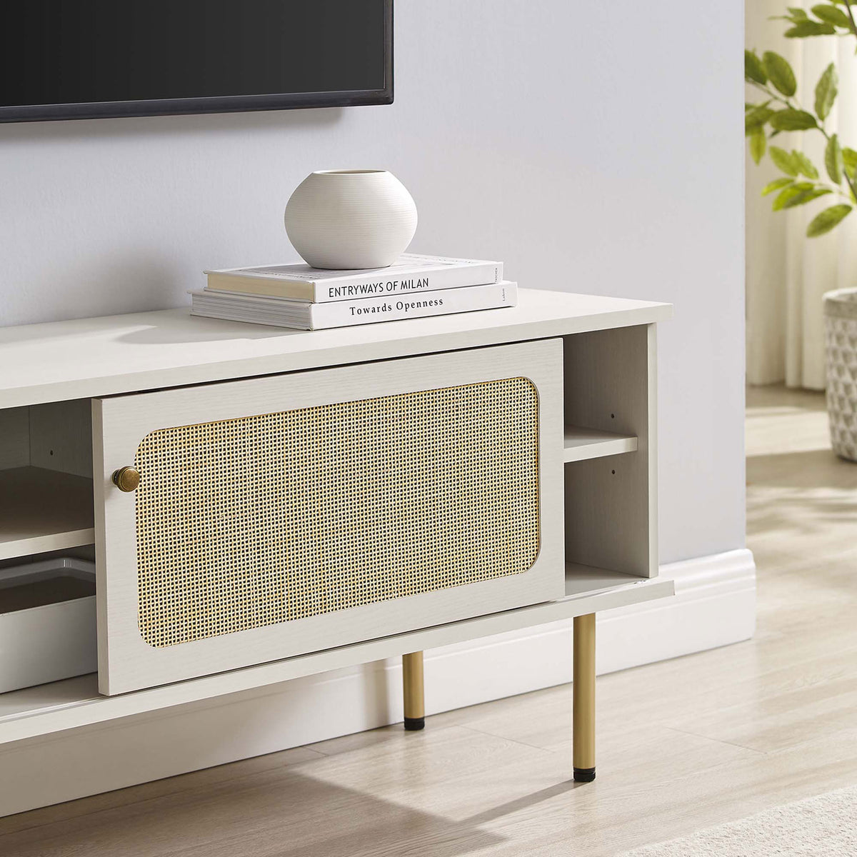 White rattan TV stand styled beneath a wall-mounted TV with books and decor in a soft-toned room. || EEI-6044-WHI || storage_room