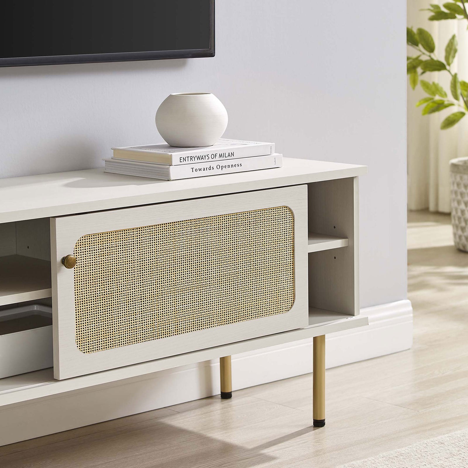White rattan TV stand styled beneath a wall-mounted TV with books and decor in a soft-toned room. || EEI-6044-WHI || storage_room