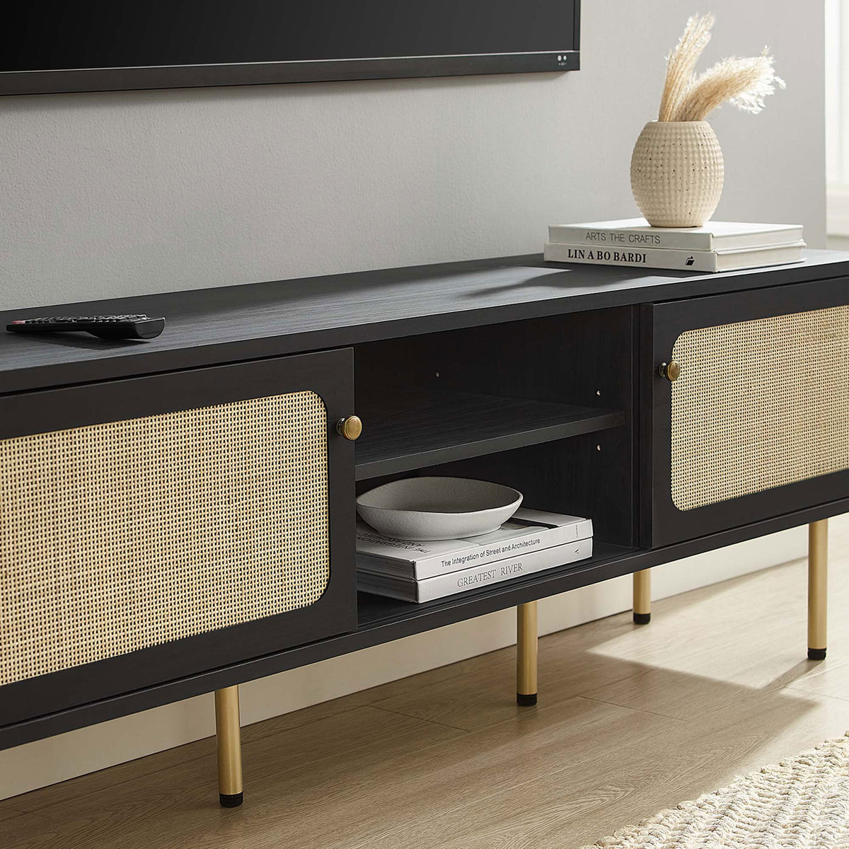 Black rattan TV stand styled under a wall-mounted TV with books and decor on the center shelf. || EEI-6045-BLK || storage_room