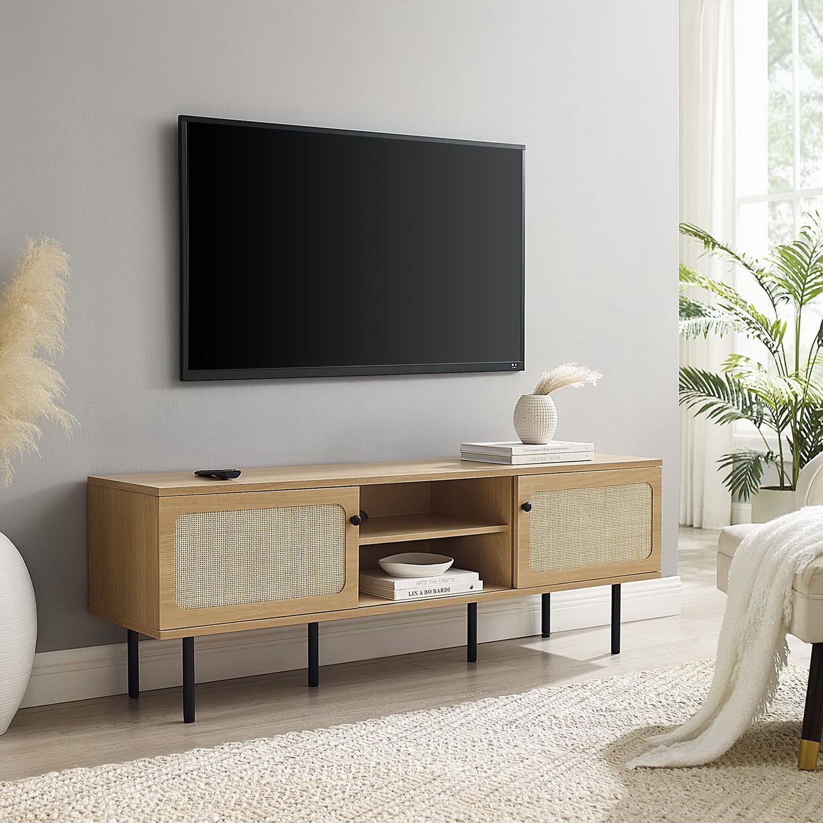 Long oak TV console with dual rattan doors and black legs grounding an airy, neutral living room. || EEI-6045-OAK || front_angle_room
