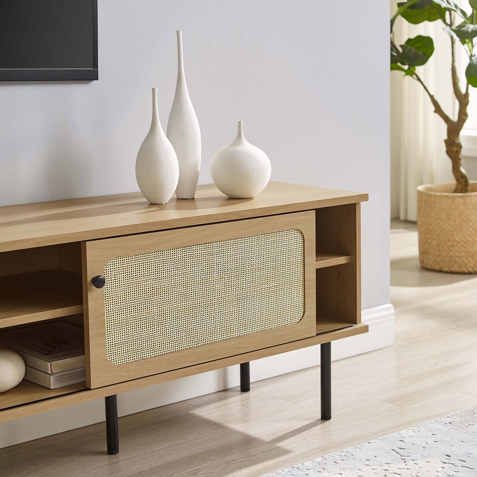 Oak rattan TV stand stretching beneath a wall-mounted TV with vases and books in a soft, modern room. || EEI-6046-OAK || storage_room