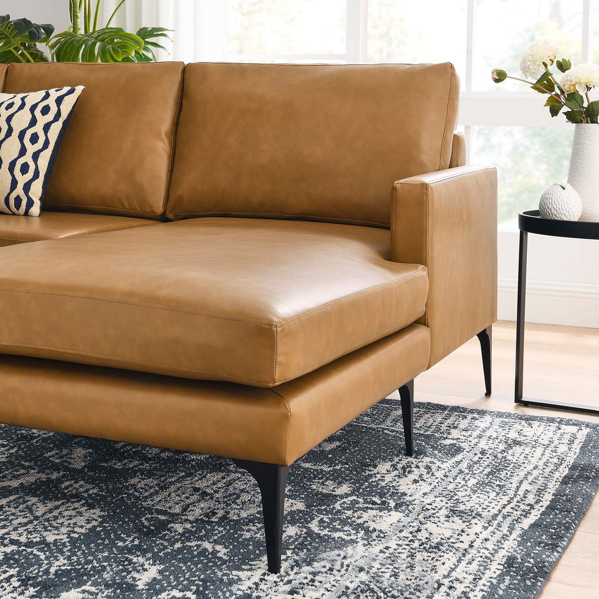 Styled tan vegan leather sectional chaise corner with black legs, navy throw pillow, and decorative rug || EEI-6050-TAN || detail_room