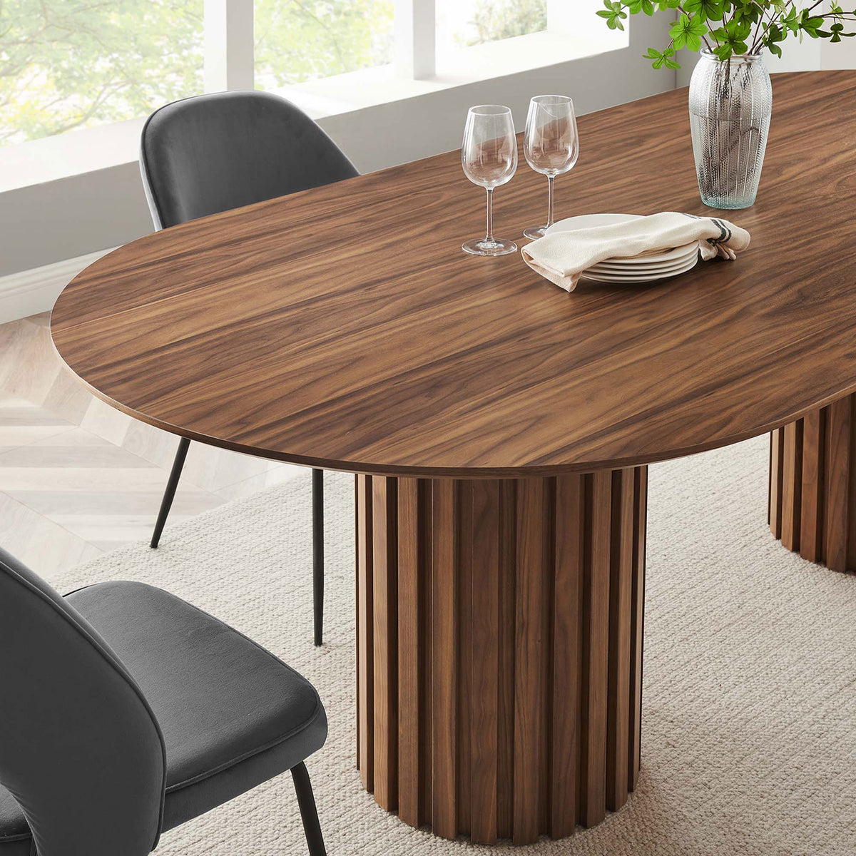 Corner of walnut oval dining table highlighting wood grain top, fluted pedestal, and contemporary place settings || EEI-6065-WAL-SET || detail_room