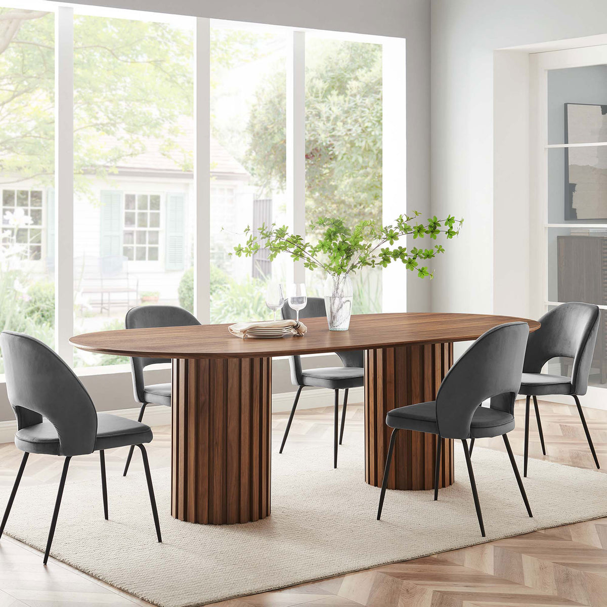 Walnut oval dining table with fluted columns styled in a bright modern dining room with four upholstered chairs || EEI-6065-WAL-SET || front_angle_room