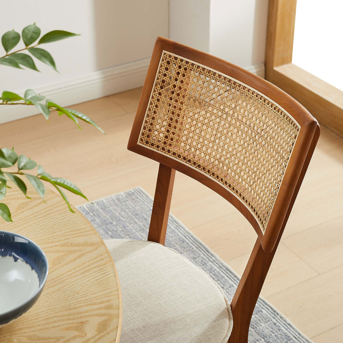 Rattan back walnut dining chair styled at a round wood table with greenery in a bright dining room. || EEI-6080-WAL-BEI || detail_room