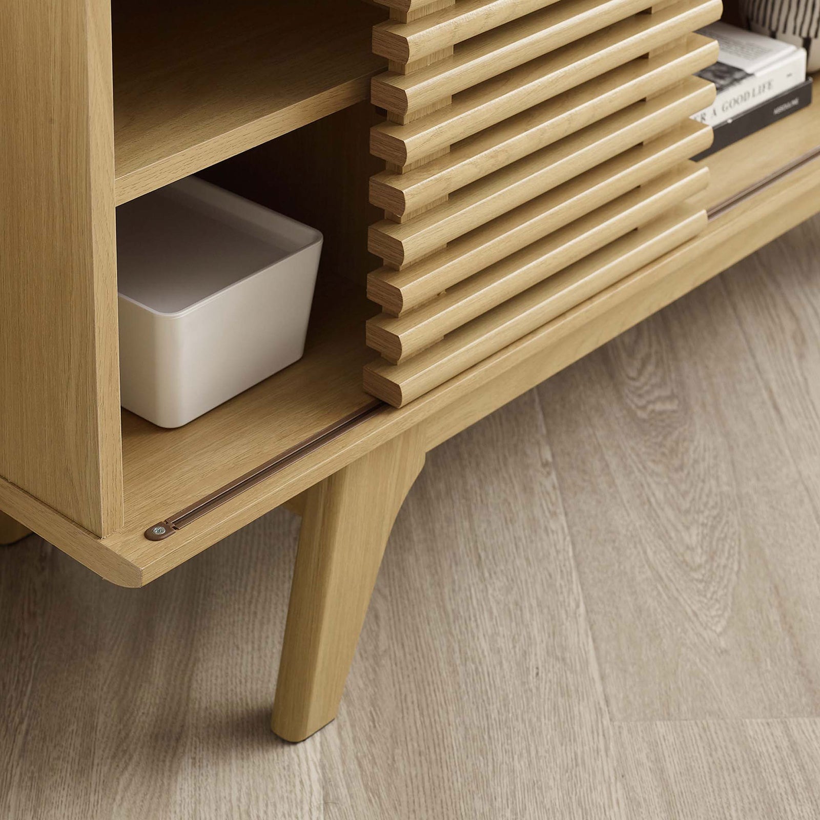 Oak TV stand shelf, slatted door edge, and tapered leg styled with decor pieces on light wood flooring || EEI-6157-OAK || detail_room