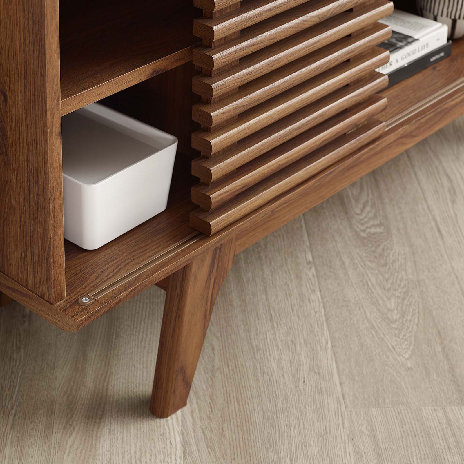 Walnut TV stand shelf, slatted door edge, and tapered leg styled with decor above pale wood flooring || EEI-6157-WAL || detail_room