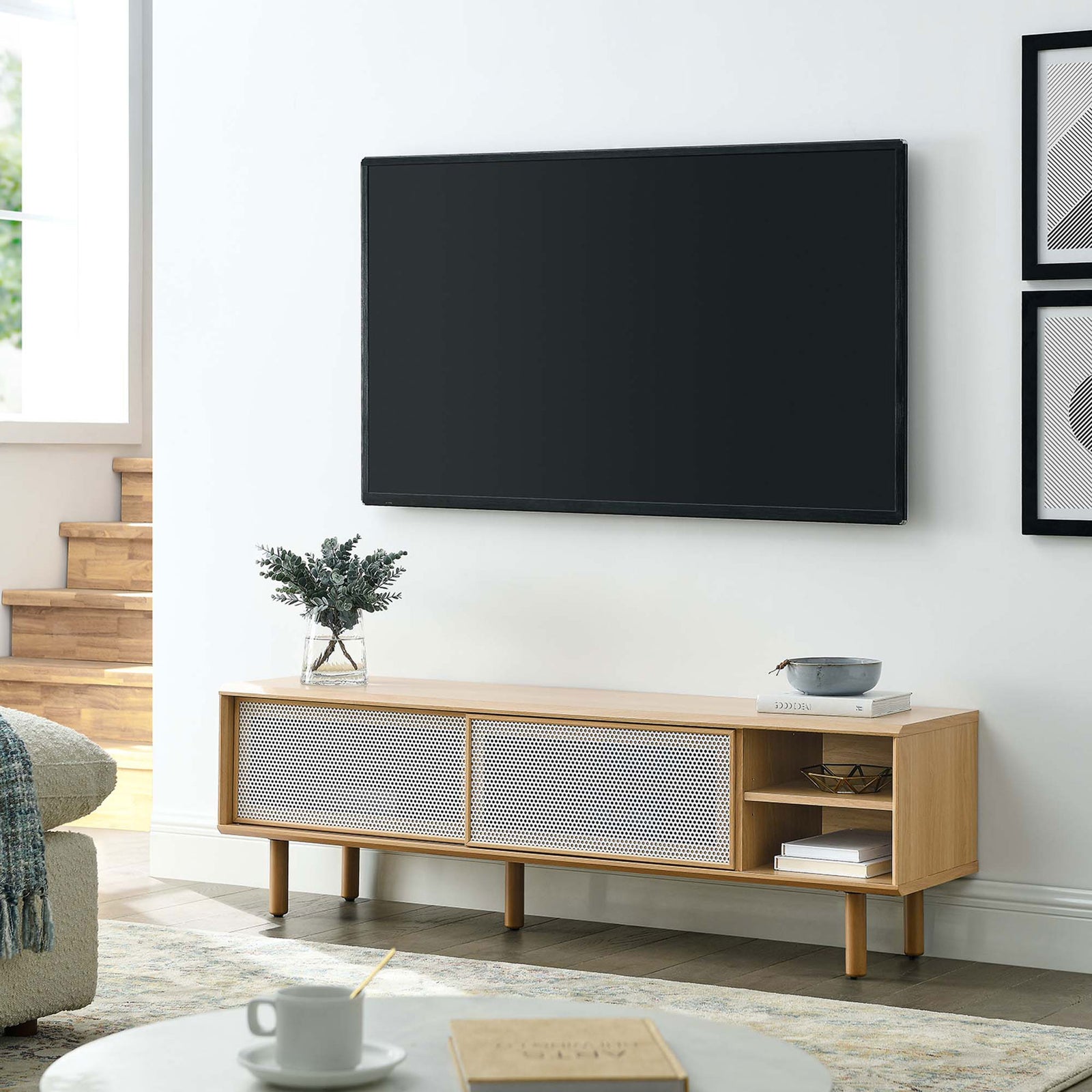 Kurtis 60 in oak TV stand in a light living room beneath a wall-mounted television || EEI-6234-OAK || front_angle_room