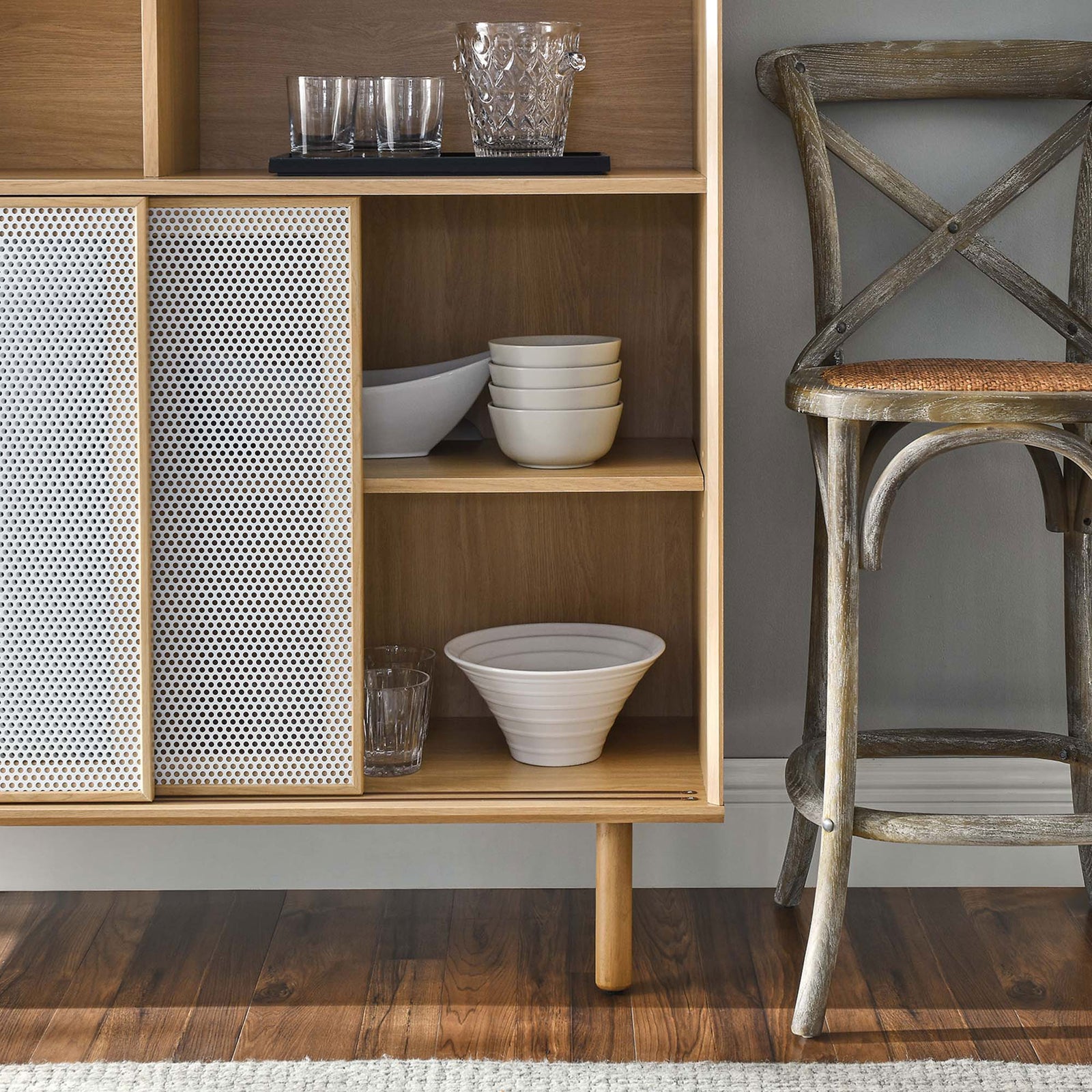 Open oak shelves neatly hold bowls and glassware, with white mesh doors adding texture to the vignette. || EEI-6237-OAK || detail_room
