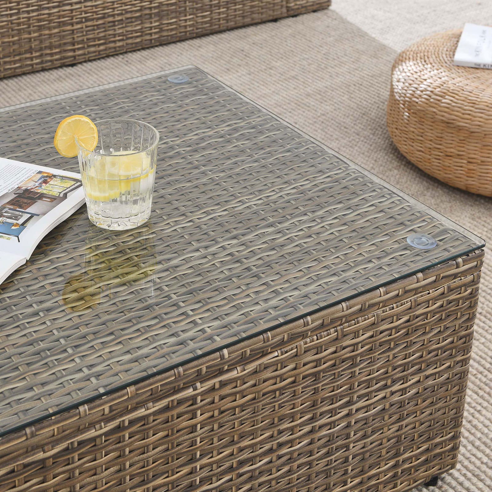 Glass-topped rattan coffee table surface styled with drink and magazine on neutral outdoor rug || EEI-6239 || detail_room