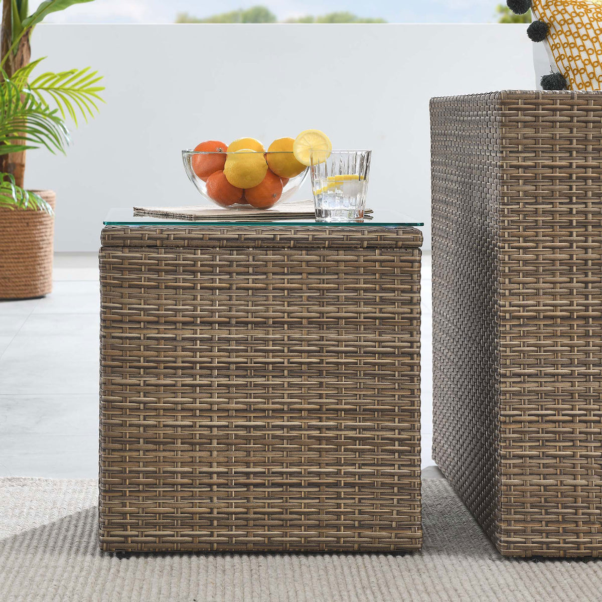 Brown rattan side table beside matching outdoor seating with glass top display surface || EEI-6240 || front_room