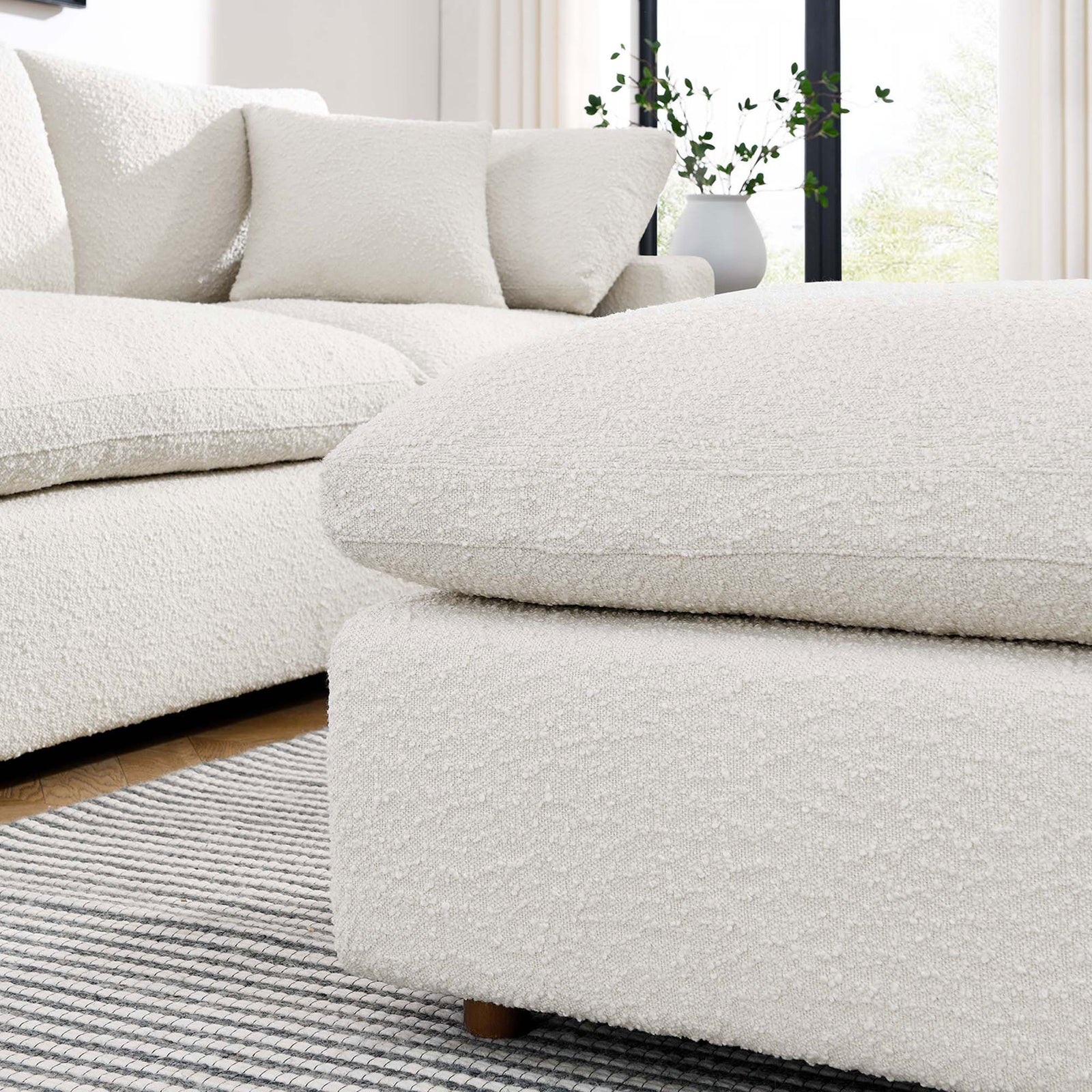 Ivory boucle ottoman layered over a striped rug, paired with a matching Commix sectional in a bright living room. || EEI-6258-IVO || front_angle_room