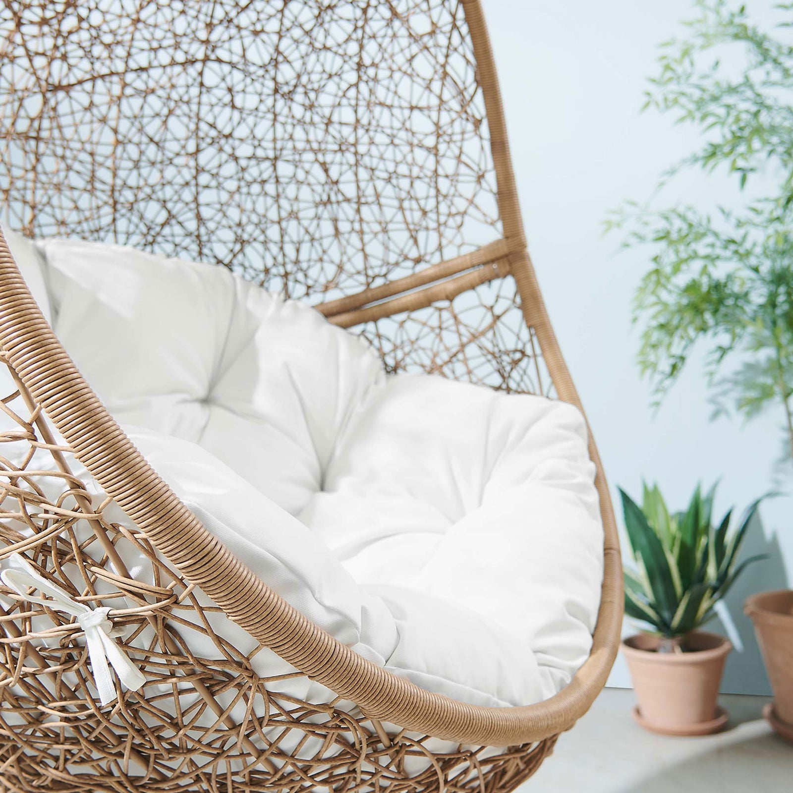 White cushioned basket swing brings resort like comfort to a light, plant filled outdoor seating area. || EEI-6262-CAP-WHI || detail_room