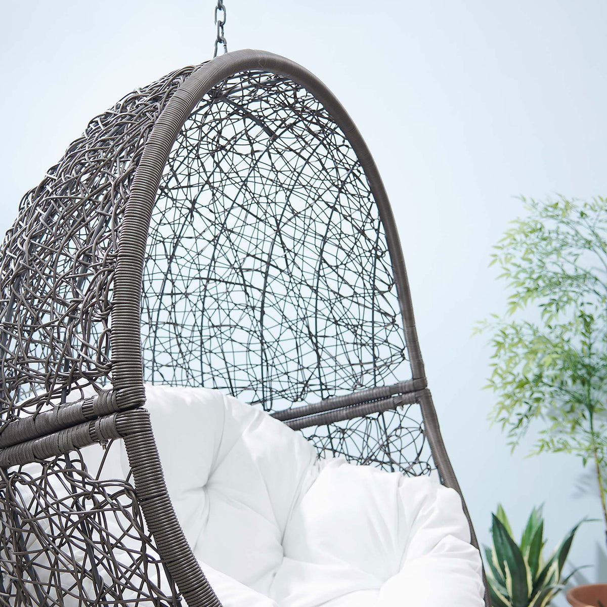 White cushioned gray rattan basket swing brings airy comfort to a modern outdoor space with plants. || EEI-6262-GRY-WHI || detail_room