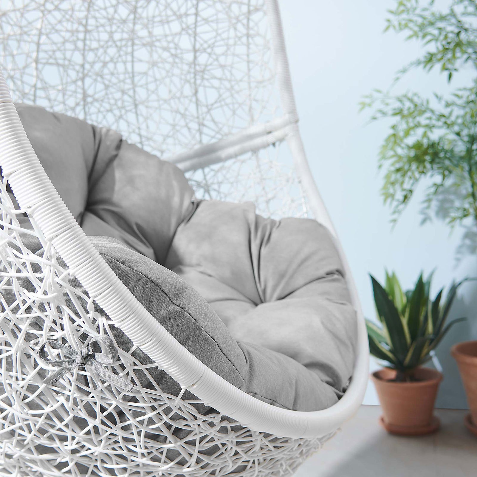 Gray cushioned basket swing adds cozy texture to an airy outdoor nook accented with potted plants. || EEI-6262-WHI-GRY || detail_room