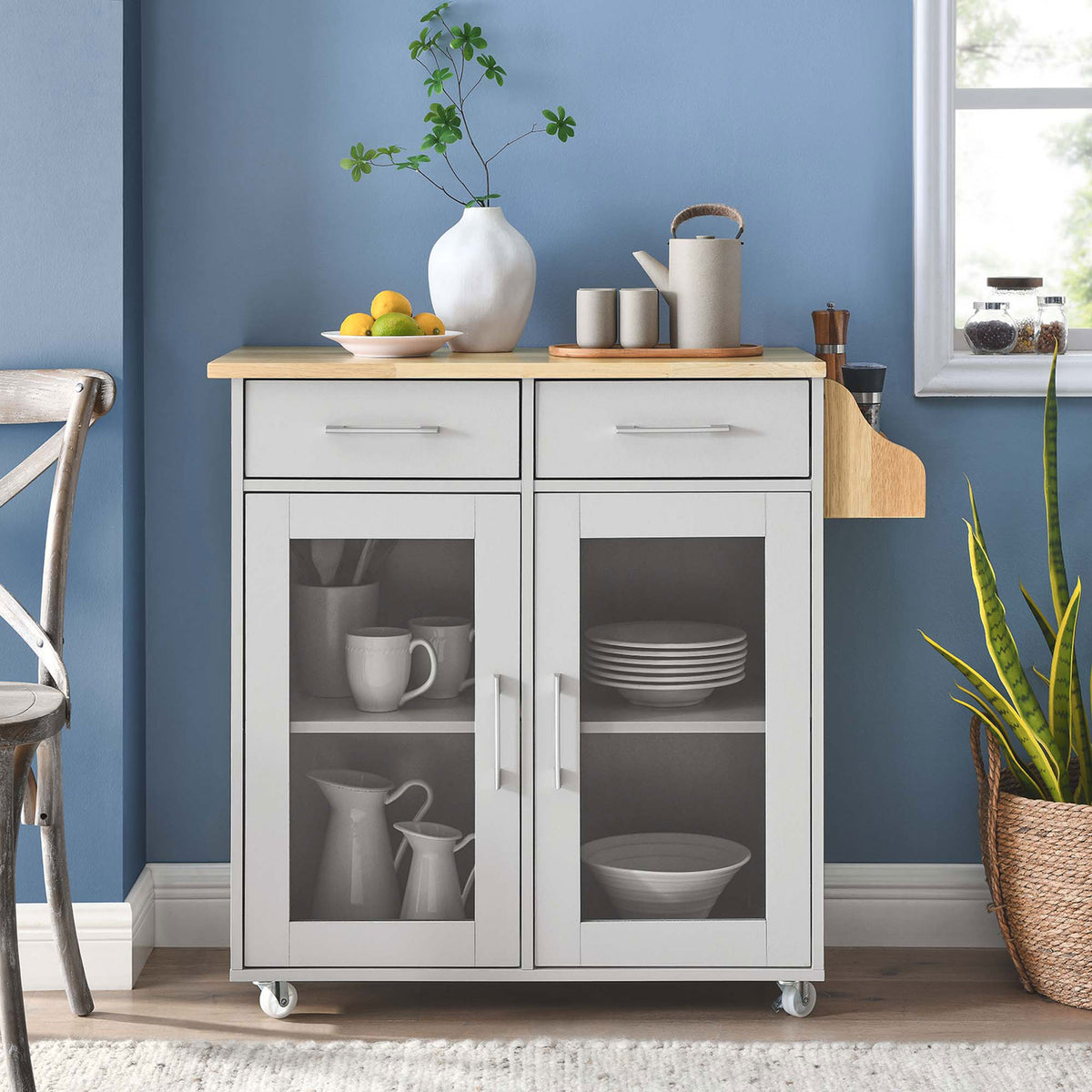 Cuisine kitchen cart styled in a bright kitchen with decor, plants, and dinnerware behind glass doors || EEI-6276-LGR-NAT || front_room
