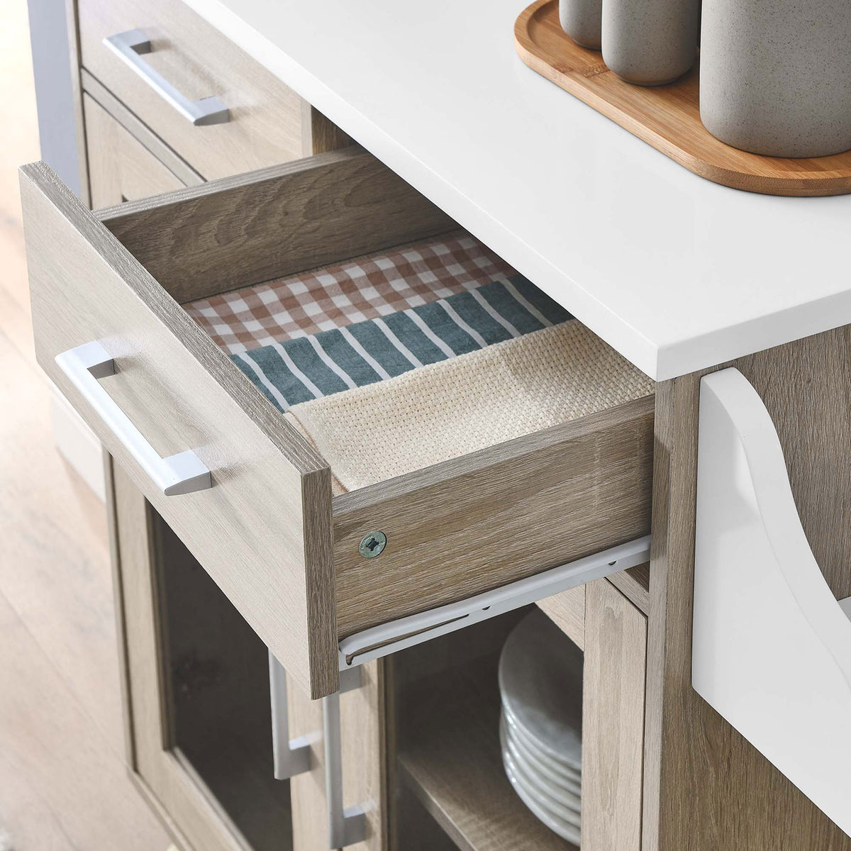 Open drawer of kitchen cart neatly storing linens beneath a smooth white work surface in a modern room || EEI-6276-OAK-WHI || storage_open_room