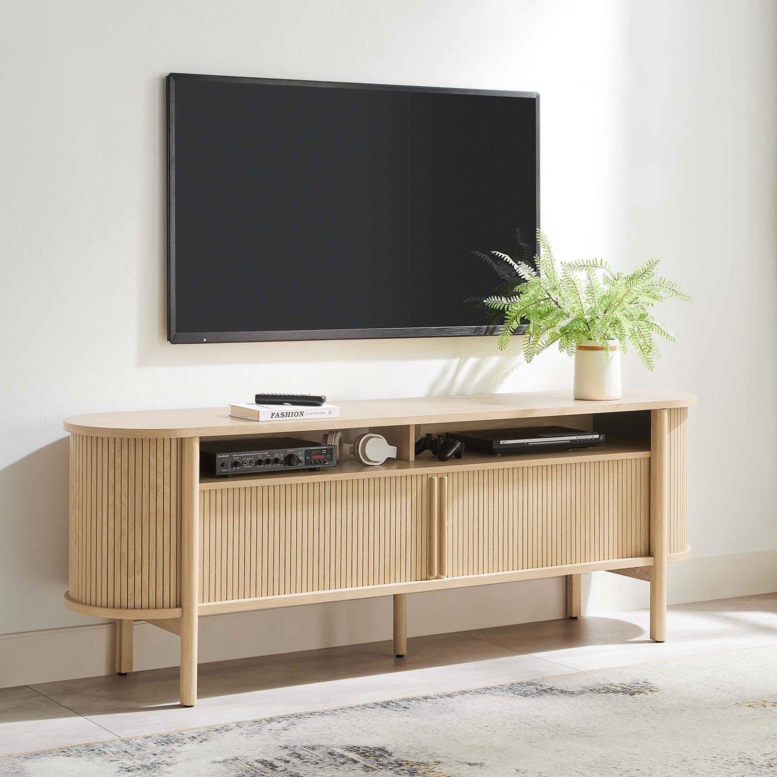 Cadence oak TV stand styled in a bright living room with wall-mounted TV and decor accents. || EEI-6310-OAK || front_angle_room