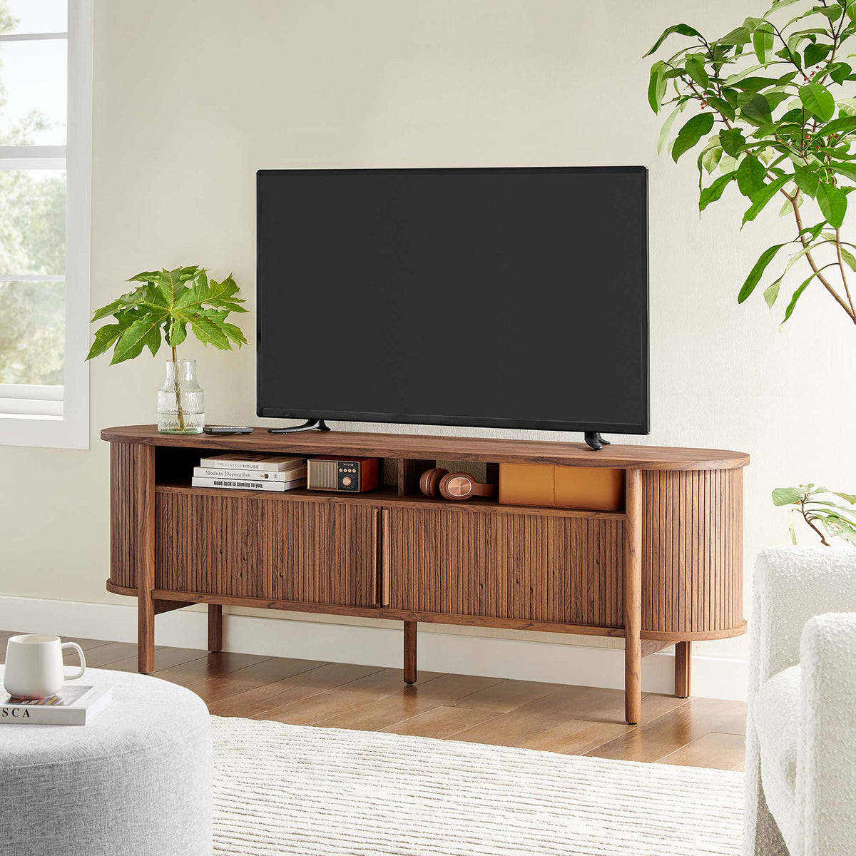 Cadence walnut TV console anchored in a cozy living room with greenery and soft seating. || EEI-6310-WAL || front_angle_room