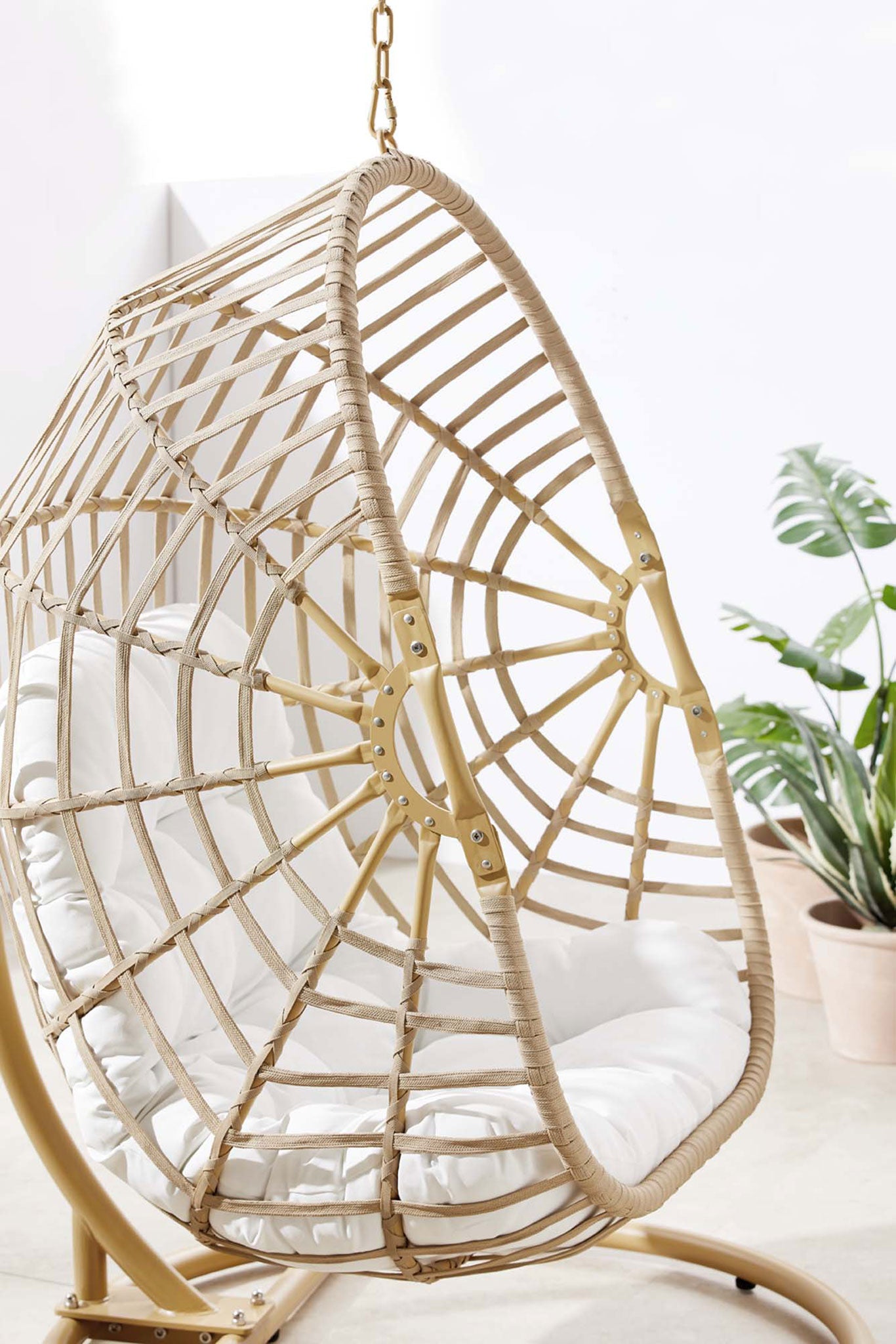 Textured rattan swing chair basket with white cushion styled with lush green potted plants in a bright space || EEI-6337-NAT-WHI || detail_room
