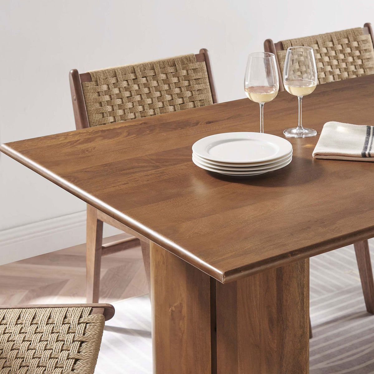 Amistad dining table corner styled with plates wine glasses and woven dining chairs || EEI-6339-WAL || detail_room
