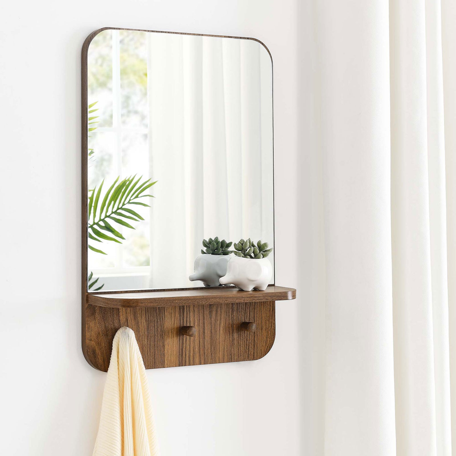 Lumina walnut wall mirror styled on a bright wall with greenery, decor, and towel on the shelf || EEI-6348-WAL || front_room