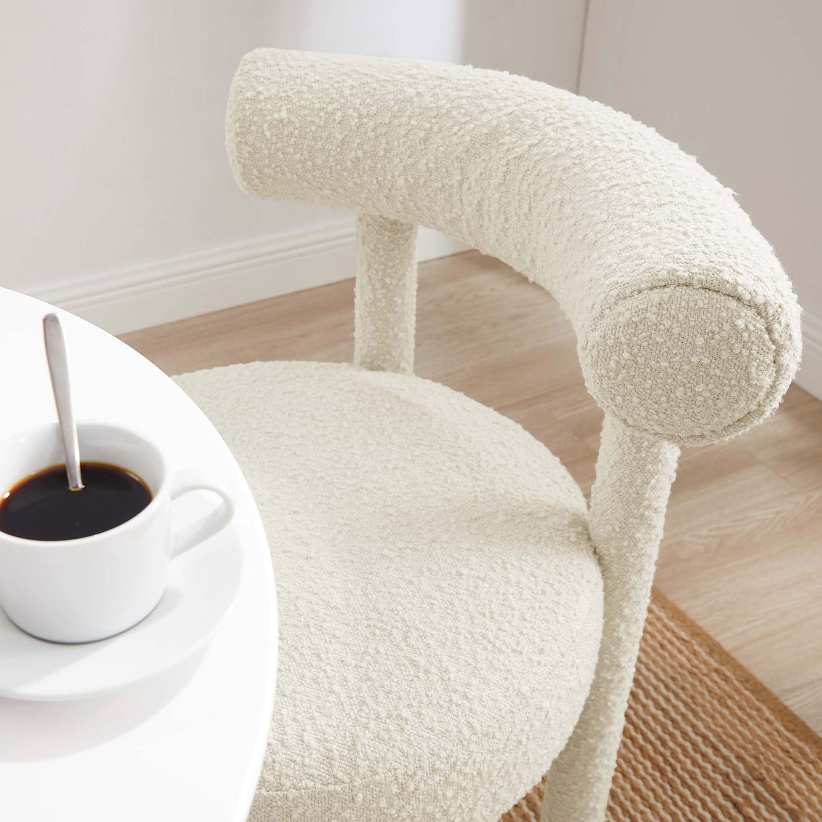 Ivory boucle dining chair pulled up to a white cafe table above a natural woven rug with coffee and decor || EEI-6387-IVO || detail_room