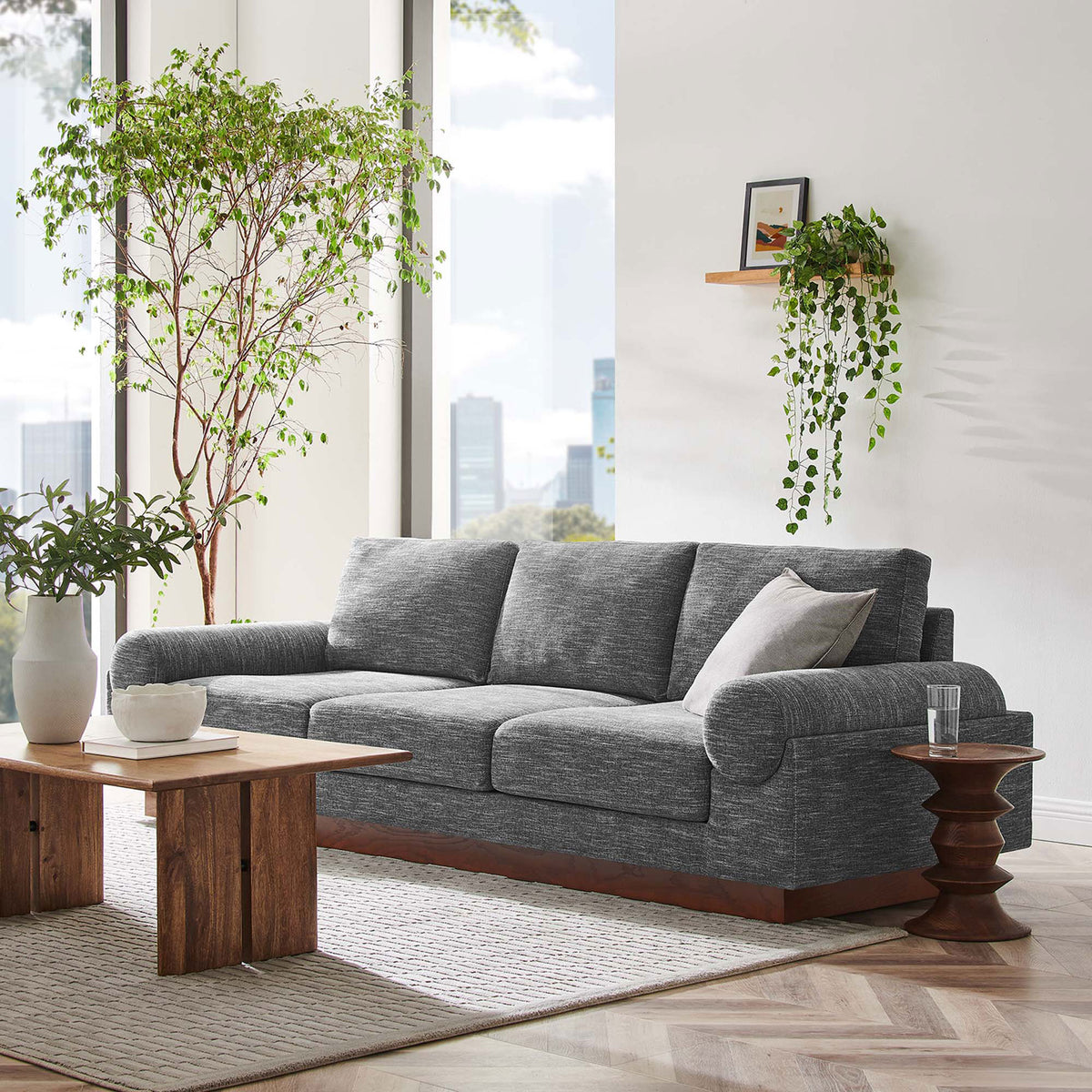 Gray Oasis sofa with wood plinth base styled with modern coffee table, plants, and city view windows || EEI-6401-GRY || front_angle_room