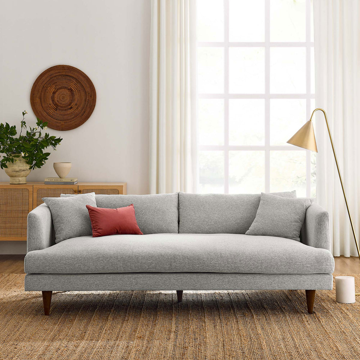 Light gray sofa in a modern living room with accent pillows, wood legs, and natural light backdrop || EEI-6405-HLG || front_room