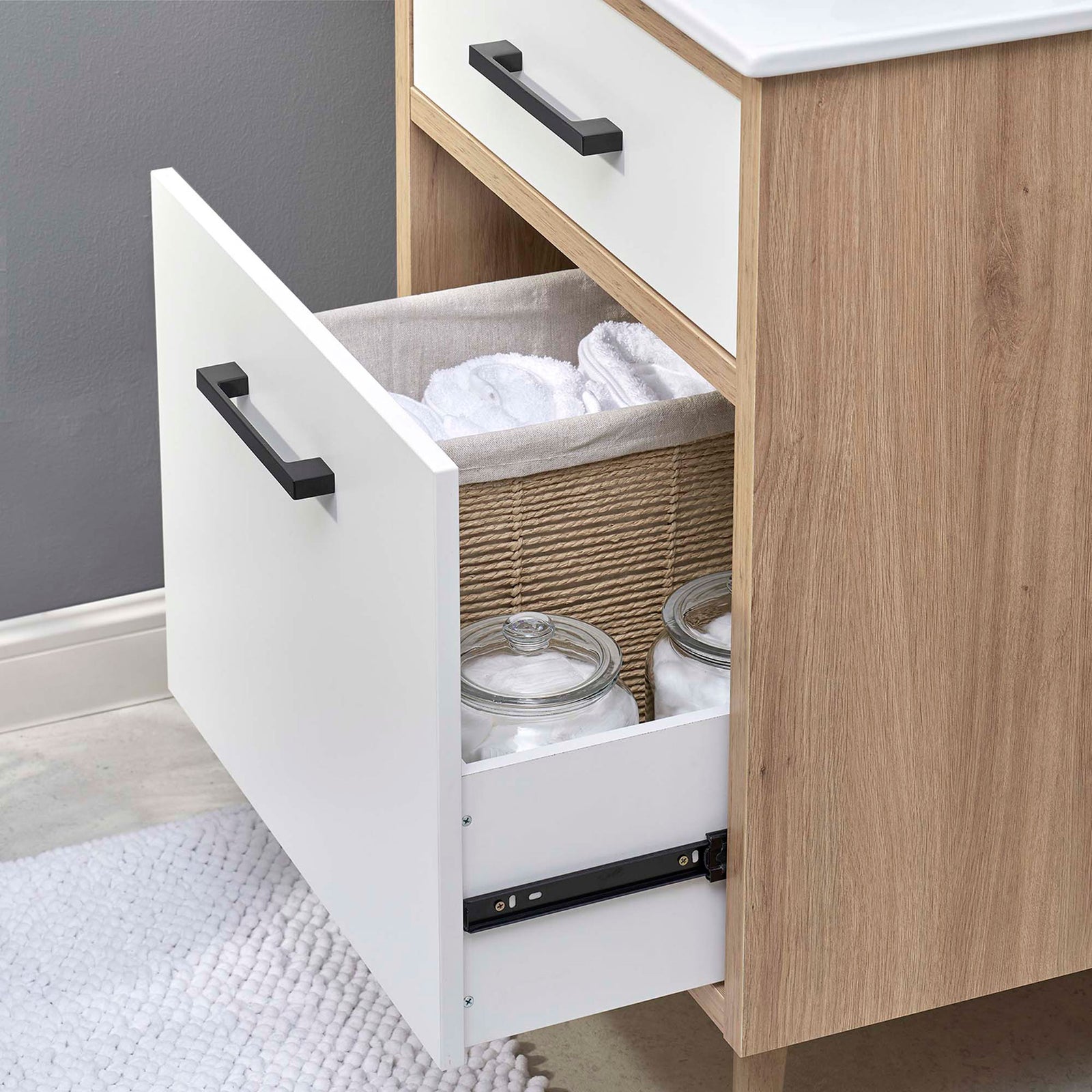 Deep lower drawer neatly organizes towels and jars within the vanity || EEI-6498-WHI-OAK || storage_open_room