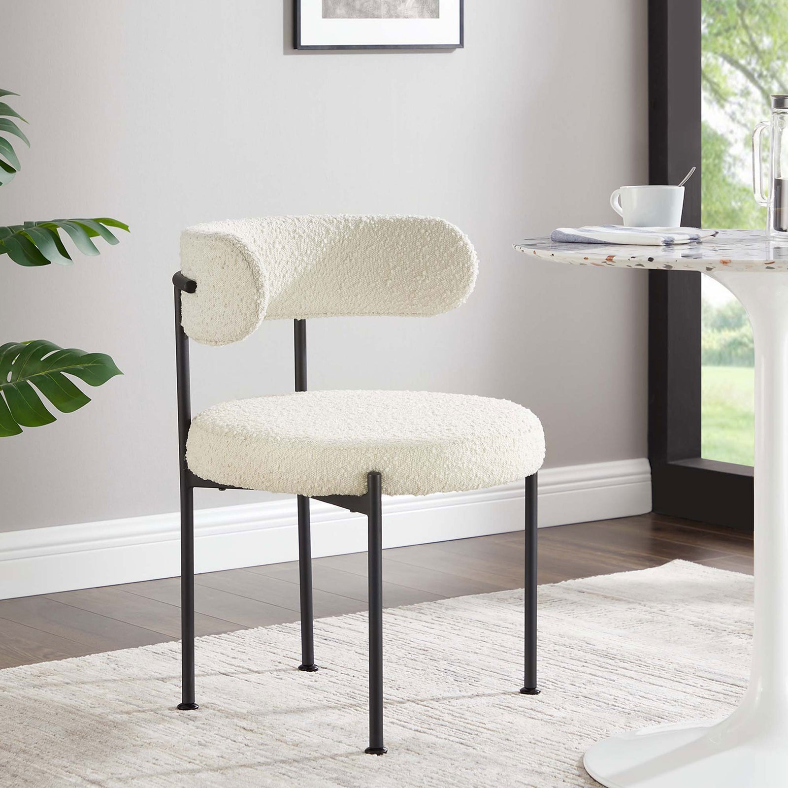 Ivory boucle dining chair styled beside a round cafe table to create a chic modern dining nook. || EEI-6516-IVO-BLK || front_angle_room