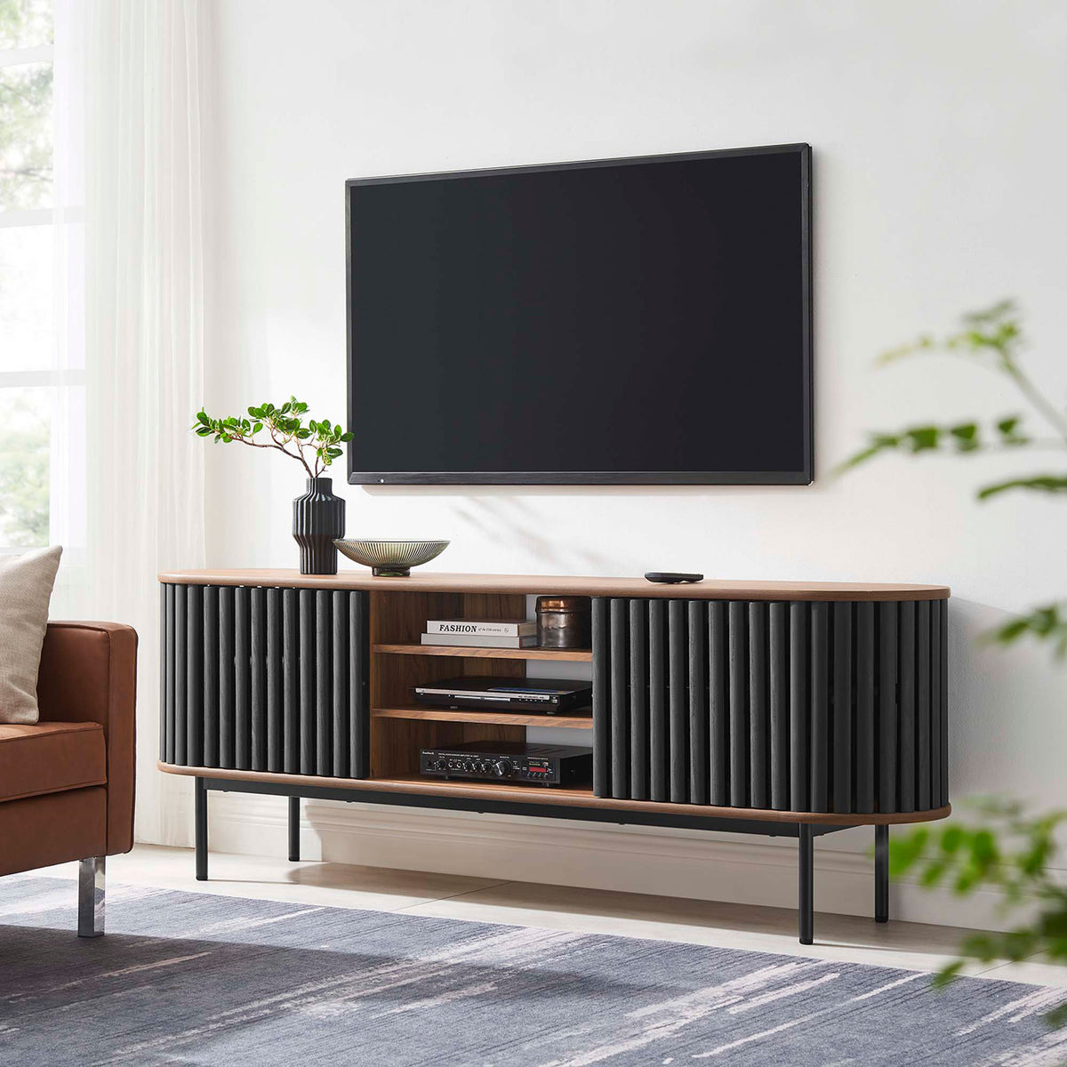 Walnut and black Fortitude TV stand anchoring a modern living room with its oval form and airy base || EEI-6522-WAL-BLK || front_room