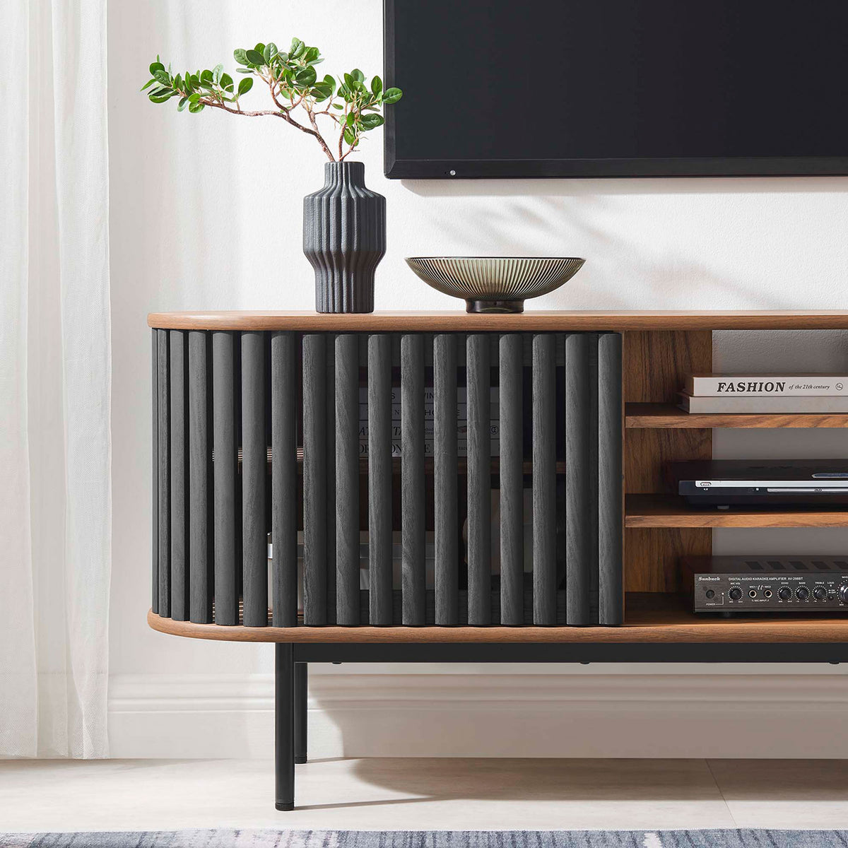 Walnut and black TV stand styled with media gear and decor below a mounted television in a bright room || EEI-6522-WAL-BLK || detail_room