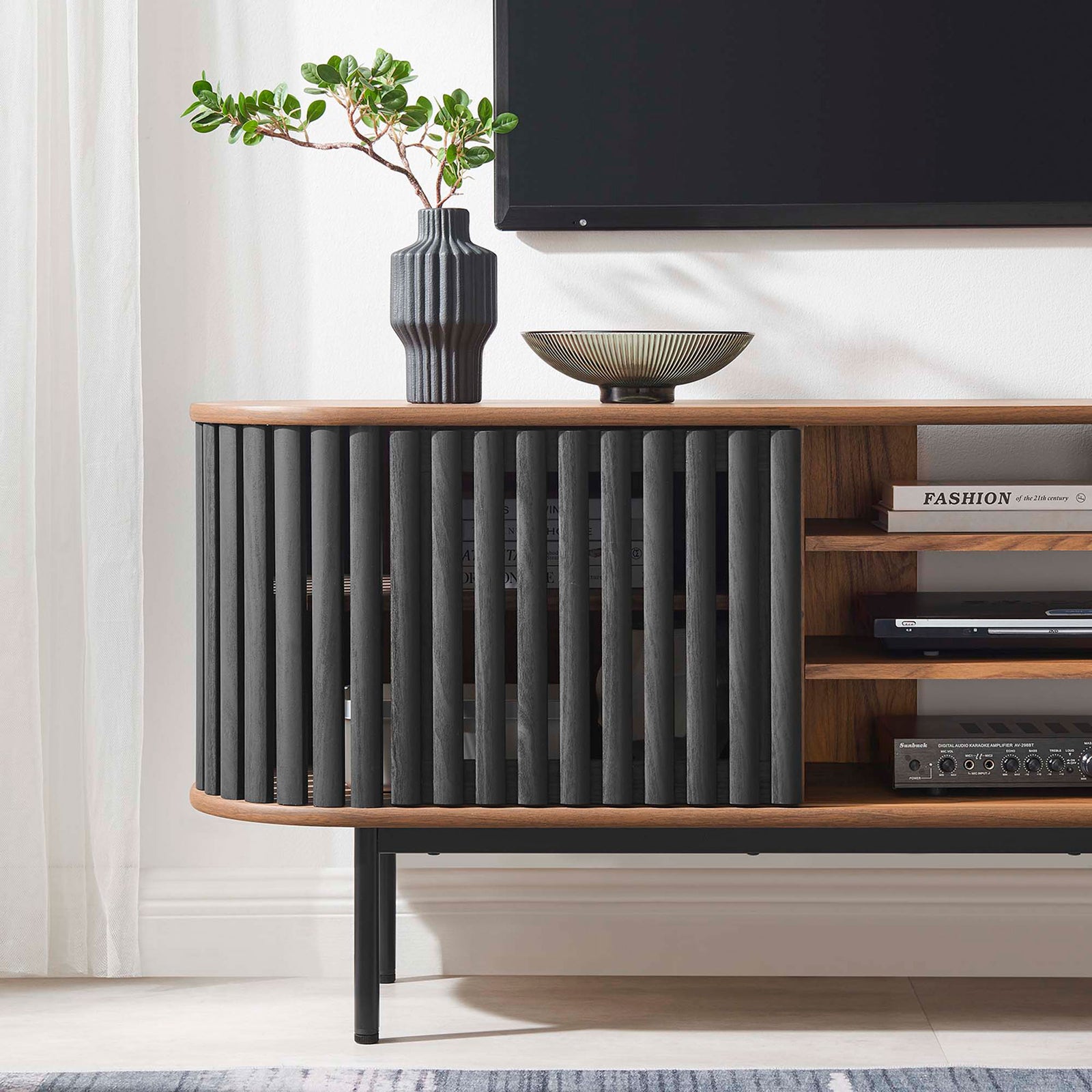 Walnut and black TV stand styled with media gear and decor below a mounted television in a bright room || EEI-6522-WAL-BLK || detail_room