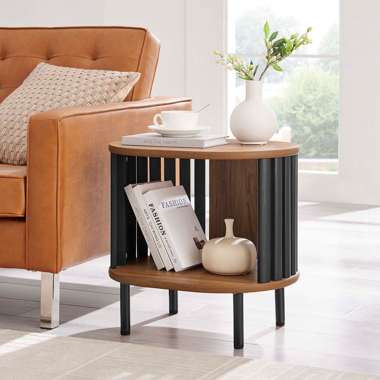 Fortitude side table beside a leather sofa, styled with books and decor on the open shelf and top || EEI-6523-WAL-BLK || front_angle_room
