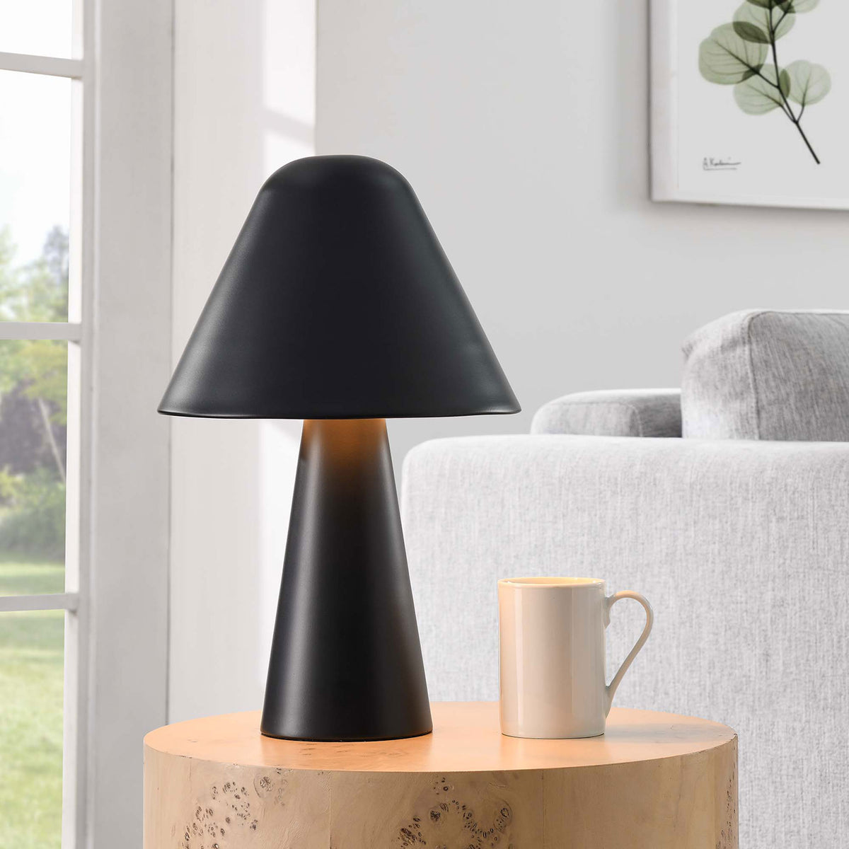 Illuminated black mushroom table lamp casts a soft glow beside a cozy contemporary sofa. || EEI-6529-BLK || front_angle_on_room