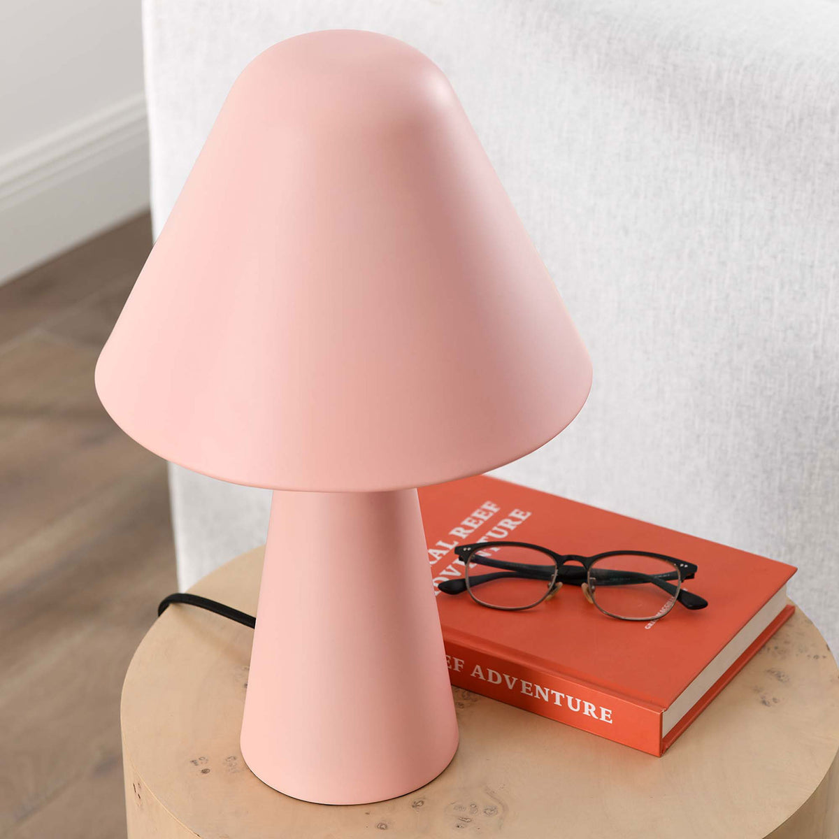 Pink Jovial mushroom lamp decorates a wood side table beside books and glasses in a bright room. || EEI-6529-PNK || top_angle_room
