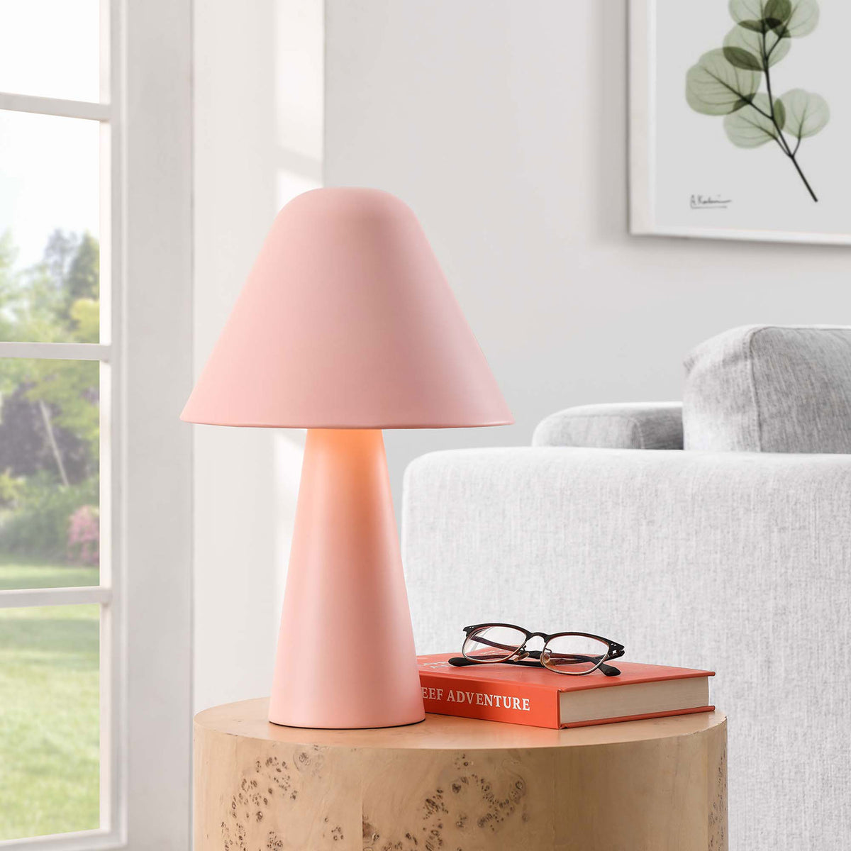 Illuminated pink mushroom table lamp adds a cozy glow next to a modern sofa and window. || EEI-6529-PNK || front_angle_on_room