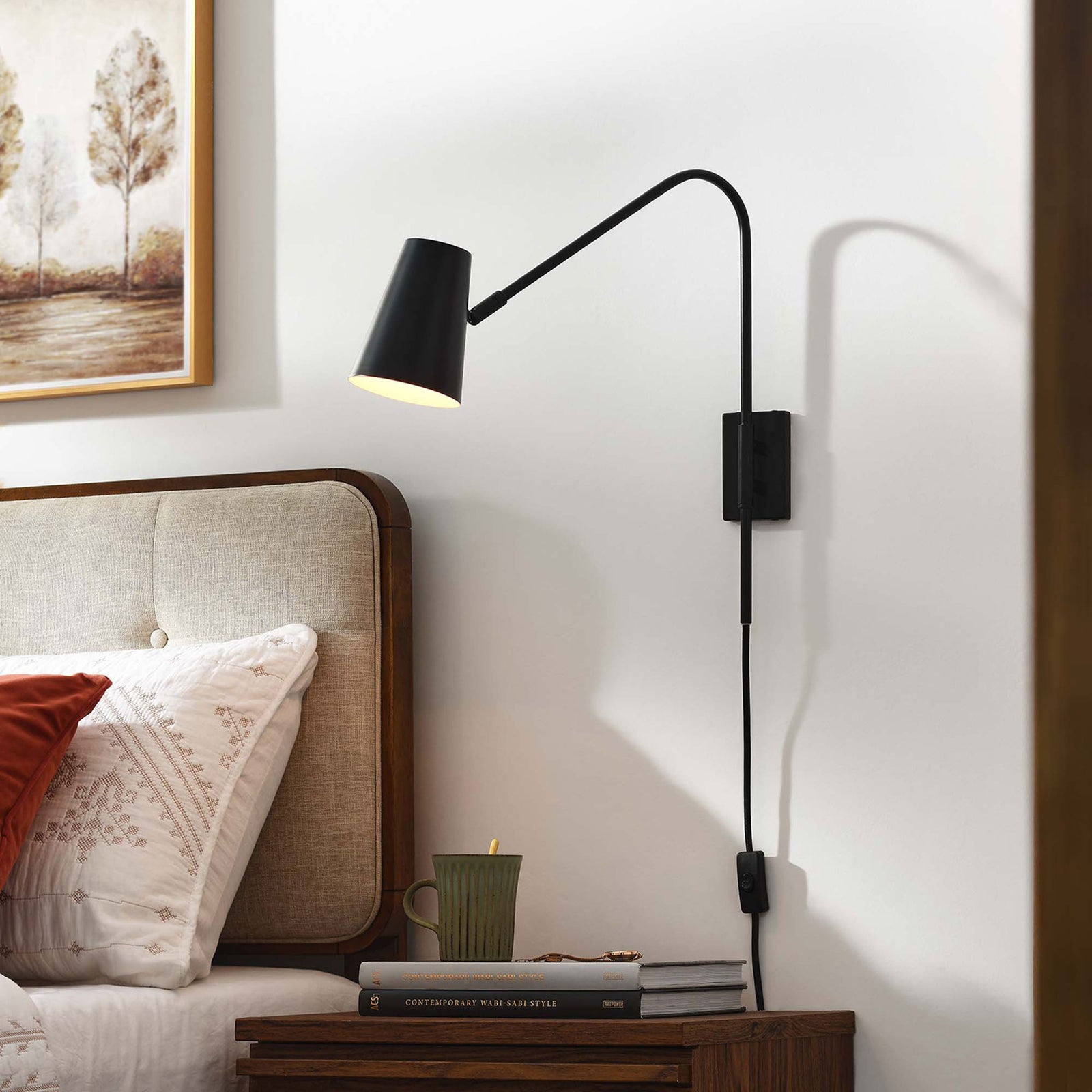 Plug in black wall sconce with fabric cord and tilting shade providing cozy light above a bedside table || EEI-6532-BLK || front_angle_on_room