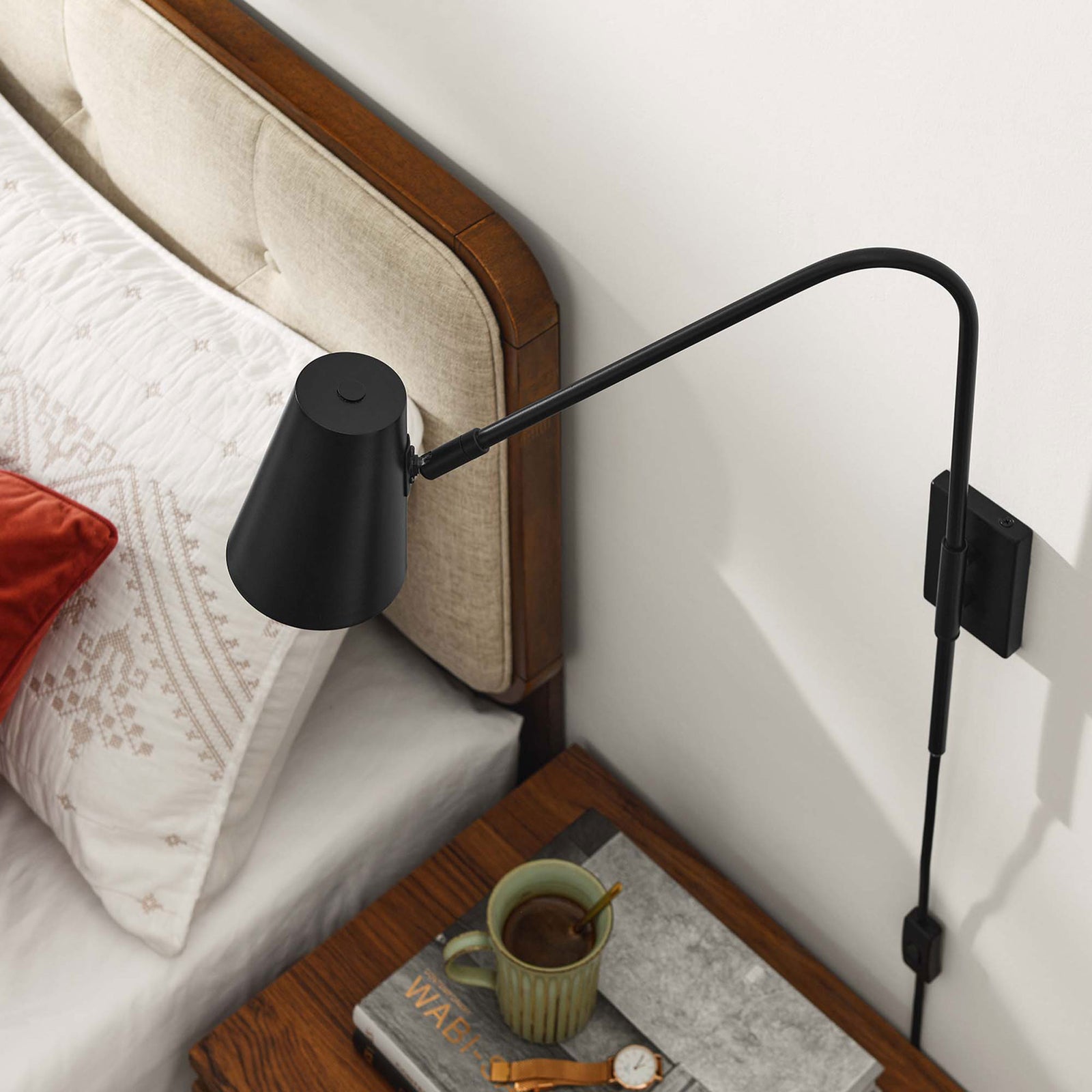 Adjustable black wall sconce reaching over a nightstand to provide focused bedside lighting || EEI-6532-BLK || top_angle_room