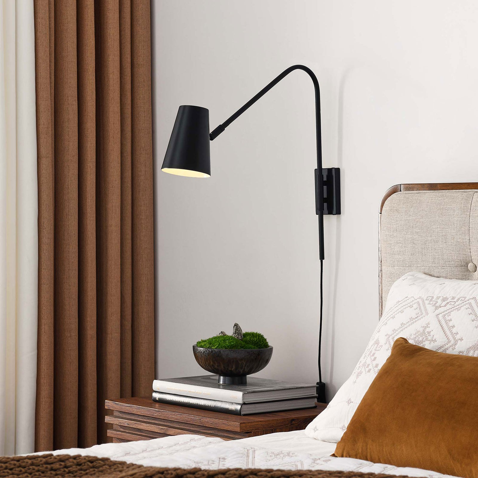Black metal wall sconce casting warm light beside the bed for modern, space saving task illumination || EEI-6532-BLK || front_angle_on_room