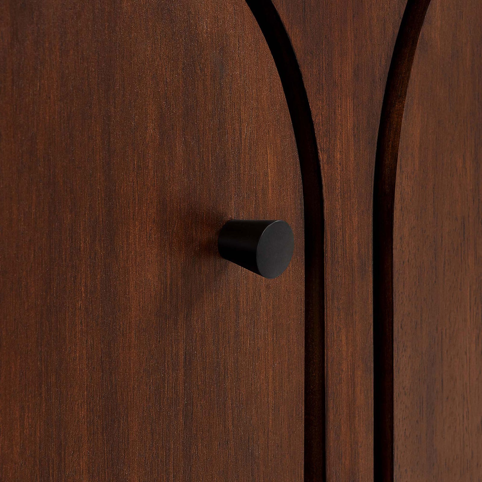 Black knob pull set against the arched walnut door, emphasizing the Appia cabinet's warm wood texture. || EEI-6536-WAL || handle_studio