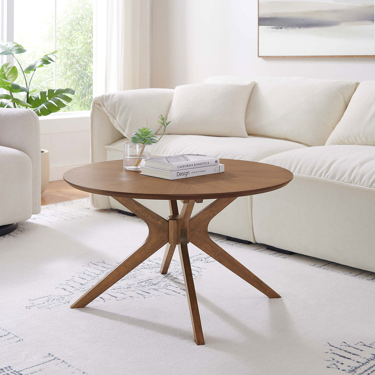 Walnut-finished round coffee table anchors a bright living space with its mid-century intersecting base. || EEI-6557-WAL || front_angle_room