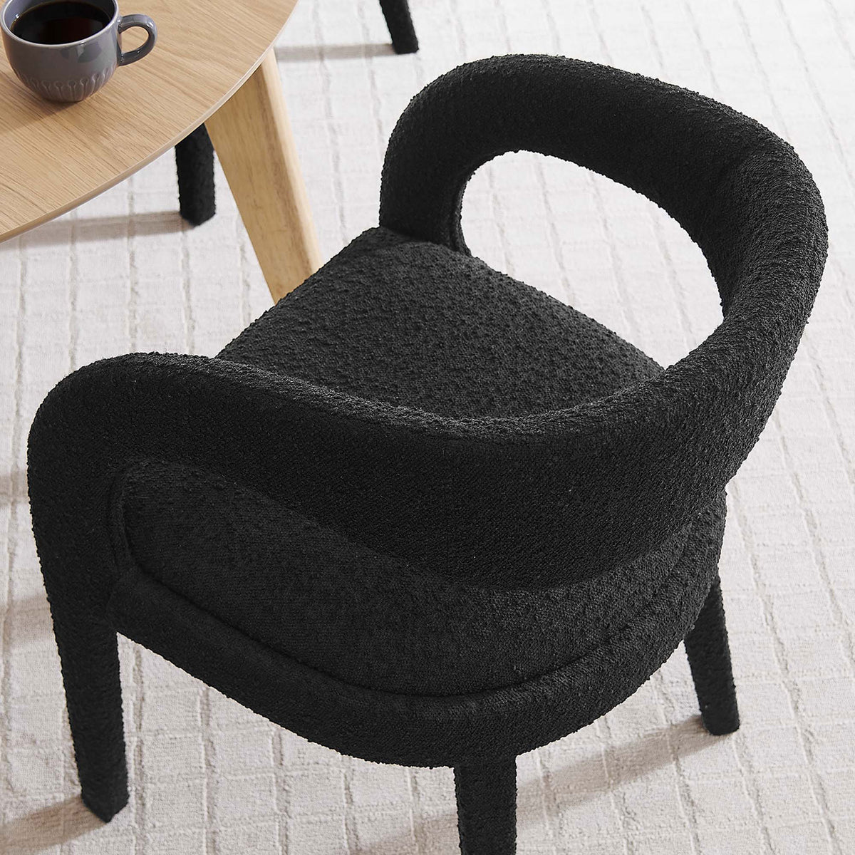 Black boucle dining chair tucked beside a light wood table, showing its rounded back in a cozy dining nook. || EEI-6562-BLK || detail_room